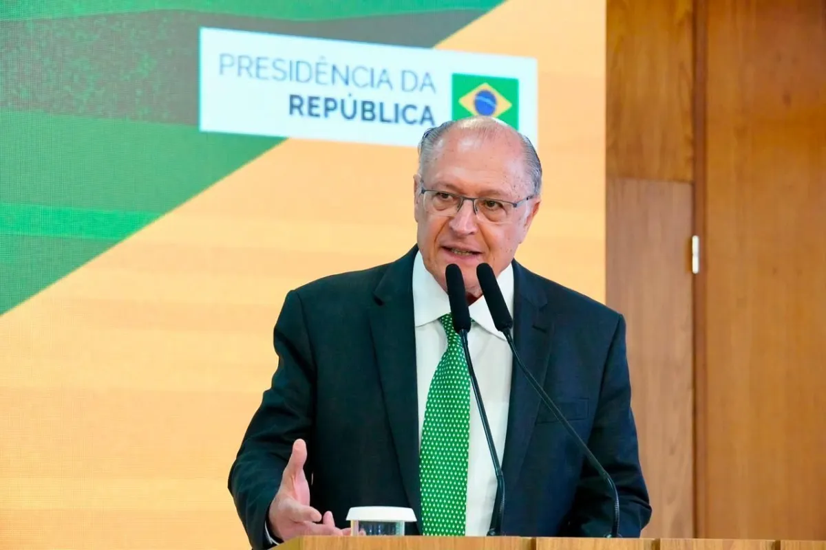 Geraldo Alckmin de terno, em evento oficial, com expressão séria e microfone à frente.