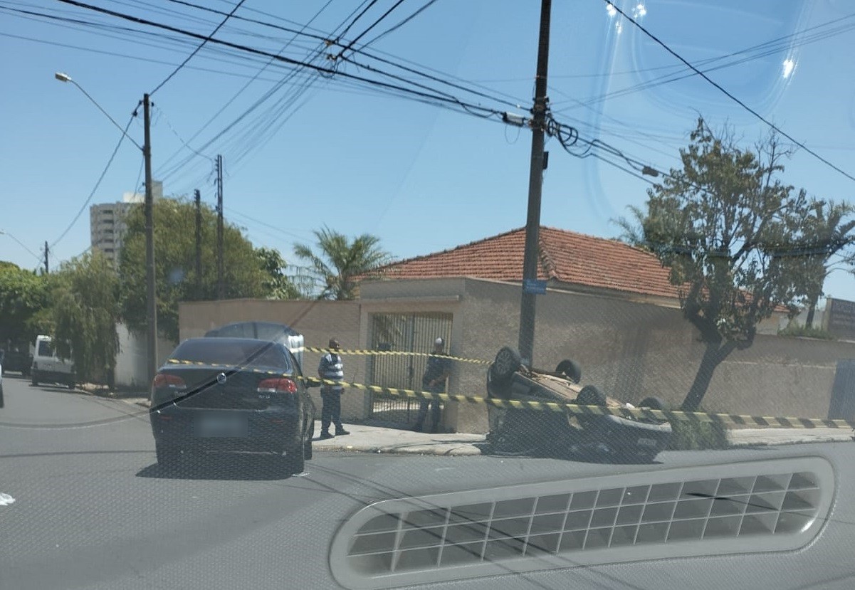Siena preto parado no cruzamento e o Uno de rodas para o alto junto a um poste, com a área isolada por fita