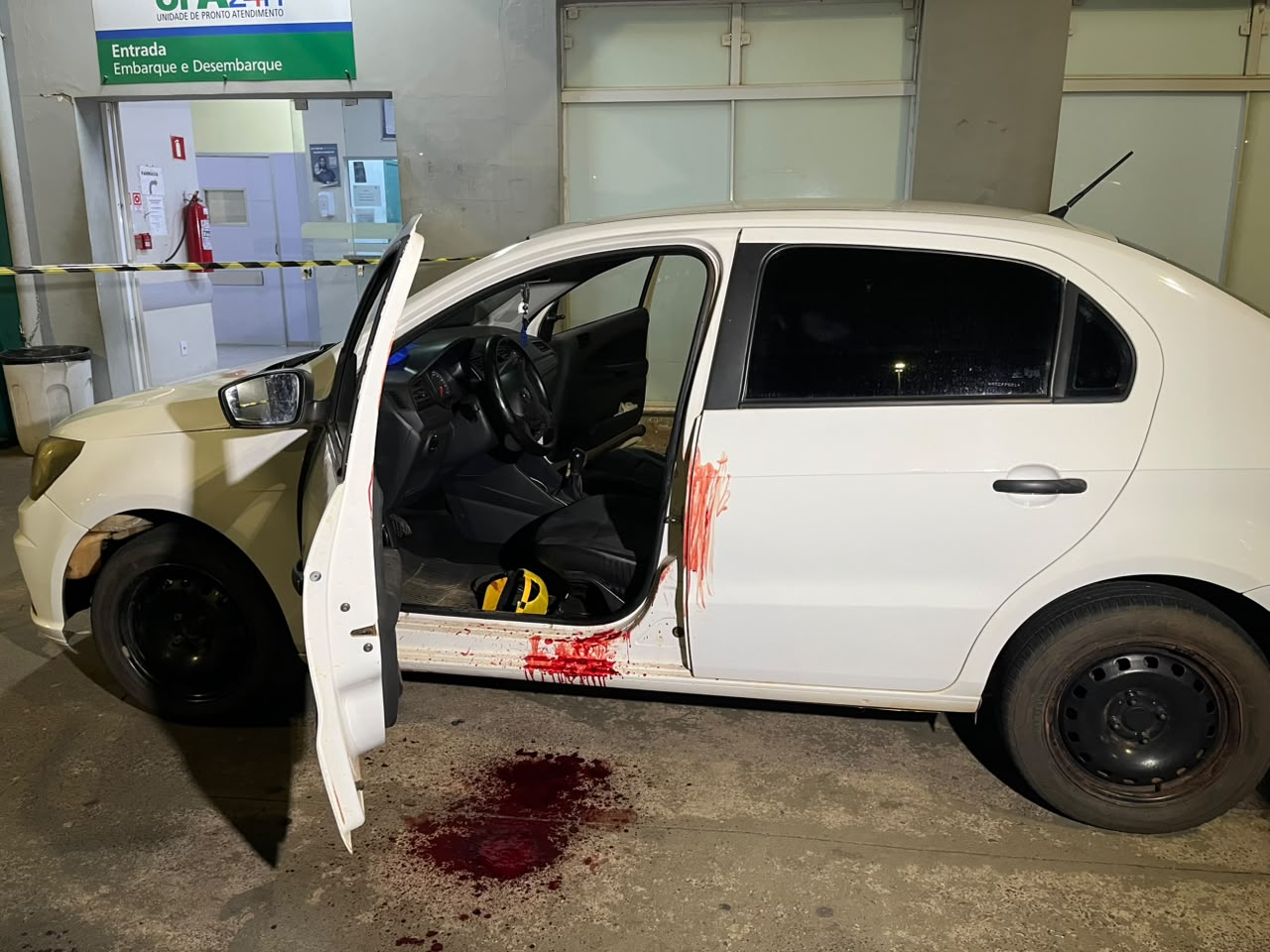 Carro branco parado em frente à UPA do Valle Verde, com manchas de sangue visíveis no banco e no interior do veículo.