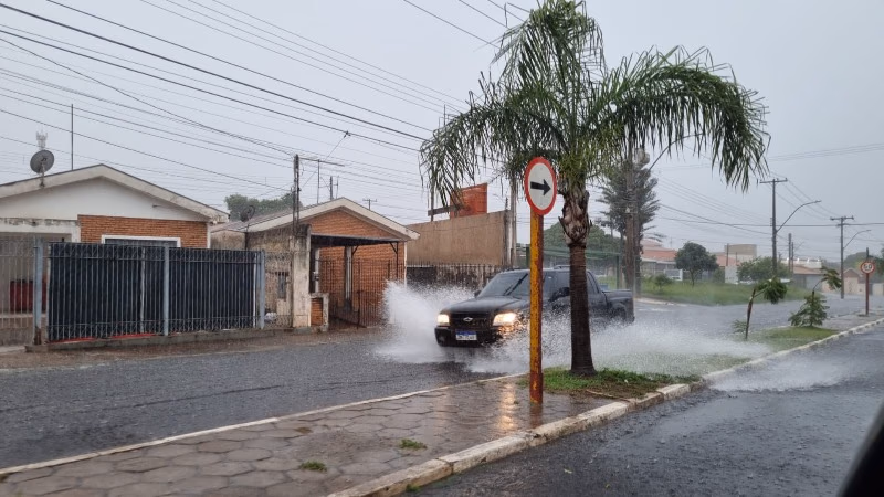 Céu nublado sobre Araraquara, com nuvens carregadas e ruas molhadas por chuva recente, visto de uma avenida arborizada
